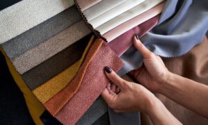 Hands feeling different textured fabric samples in warm, neutral colors.